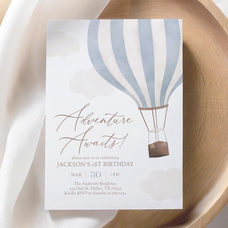 Puede incluir: Un globo aerost&aacute;tico azul y blanco a rayas con nubes y el texto "Adventure Awaits!"  Por favor, &uacute;nase a nosotros para celebrar el primer cumplea&ntilde;os de Jackson.  El 30 de marzo a la 1:00 PM.  The Anderson Residence, 234 Oak St, Dallas, TX 76543.  Por favor, confirme su asistencia a Natalie al 765.1234.