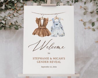 May include: Welcome to Stephanie & Micah's Gender Reveal on September 21, 2024. A sign with a watercolor illustration of a brown baby girl outfit and a blue baby boy outfit hanging on a clothesline.
