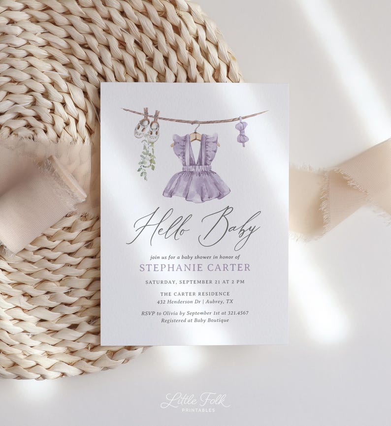 May include: A baby shower invitation with a watercolor design. The invitation features a purple dress, baby shoes, and a bow hanging on a clothesline. The text reads "Hello Baby" and includes event details.