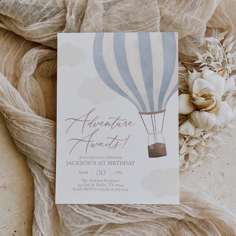Puede incluir: Un globo aerost&aacute;tico azul y blanco a rayas con una cesta marr&oacute;n, rodeado de nubes blancas. El texto "Adventure Awaits!" est&aacute; escrito en cursiva. La invitaci&oacute;n dice "Por favor, &uacute;nase a nosotros para celebrar el primer cumplea&ntilde;os de Jackson. Mar 30 | 1 PM. The Anderson Residence, 234 Oak St, Dallas, TX 76543. Por favor, RSVP a Natalie al 765.1234."