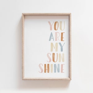 May include: A framed print with the text "You are my sunshine" in a colorful, watercolor-style font. The words are arranged vertically in a rainbow of colors, including pink, orange, yellow, blue, and green.