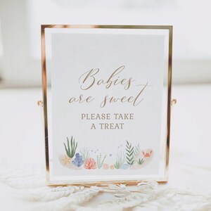 May include: A gold-framed sign with the text "Babies are sweet" and "Please take a treat". The sign is decorated with a watercolor illustration of seashells, coral, and seaweed.