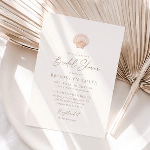 May include: A cream-coloured bridal shower invitation featuring a seashell graphic. The invitation includes the text "Bridal Shower" and details for Brooklyn Smith's shower, including the date, time, and location. A palm leaf is in the background.