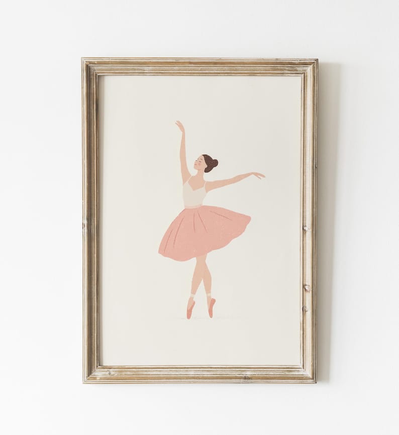 May include: A framed print featuring a ballerina in a graceful pose. The illustration depicts a dancer in a white leotard and a pink tutu, with arms extended. The artwork is set against a neutral background, framed in a light-toned wooden frame.
