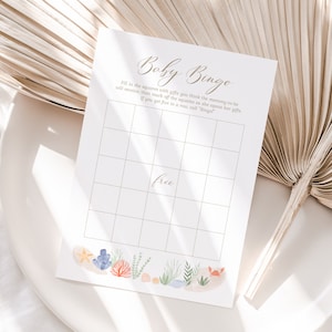 Peut inclure: Une carte de bingo de baby shower imprimable avec un fond brun clair et une grille blanche. La carte a un titre qui dit "Baby Bingo" et des instructions pour remplir les cases avec les cadeaux que la future maman recevra. La carte a également une case gratuite au centre et une bordure d'illustrations de la vie marine.