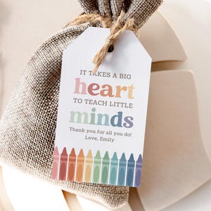 May include: A gift tag with the text "IT TAKES A BIG heart TO TEACH LITTLE minds" and a row of colorful crayons at the bottom. The tag says "Thank you for all you do! Love, Emily".