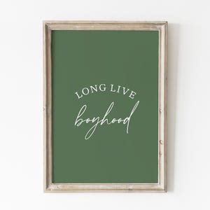 May include: Framed wall art with a green background and the words "LONG LIVE boyhood" in white script. The frame is a light, neutral color, and the artwork is displayed against a white wall.
