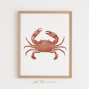 May include: A framed wall art print featuring a watercolor illustration of a terracotta-colored crab centered on a white background. The light wood frame surrounds the artwork, and the text Little Folk PRINTABLES is printed at the bottom.