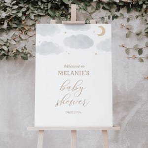 May include: A white welcome sign with a watercolor sky background featuring clouds and stars. The text reads "Welcome to Melanie's Baby Shower 06.12.2024".