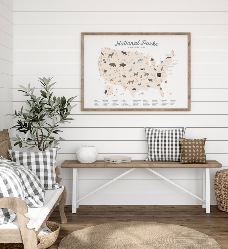 Puede incluir: Un mapa enmarcado de los Estados Unidos con fondo beige y borde marr&oacute;n. El mapa muestra la ubicaci&oacute;n de todos los parques nacionales de los Estados Unidos. Cada parque est&aacute; marcado con un peque&ntilde;o icono que representa un animal nativo de ese parque. El mapa est&aacute; colgado en una pared blanca con paneles de madera blanca. Debajo del mapa hay un banco de madera con dos almohadas, un jarr&oacute;n de cer&aacute;mica blanco y una peque&ntilde;a caja de madera.
