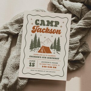May include: A rectangular birthday invitation card with a wavy border, featuring the text CAMP JACKSON in green and orange. The design includes a tent, pine trees, and mountains. Details include June 15, Jackson's 5th birthday, and address.