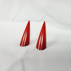 Könnte beinhalten: Zwei rote, kegelförmige, dekorative Hörner. Die Hörner bestehen aus einem glatten, glänzenden Material.