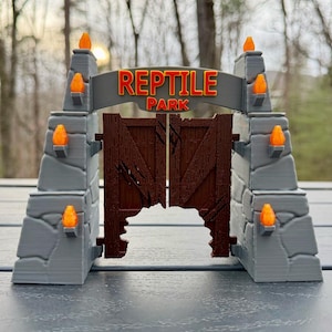 Könnte beinhalten: Ein Miniatur-Eingangstor zum Reptilienpark. Das Tor hat eine graue Steinfassade mit orangefarbenen, flammenförmigen Lichtern und ein braunes Holztor. Das Schild darüber trägt die Aufschrift "REPTILE PARK" in Rot und Gelb.