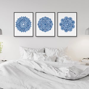 May include: Three framed prints of blue and white mandala designs on a white wall above a white bed with white bedding.