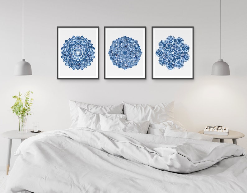 May include: Three framed prints of blue and white mandala designs on a white wall above a white bed with white bedding.