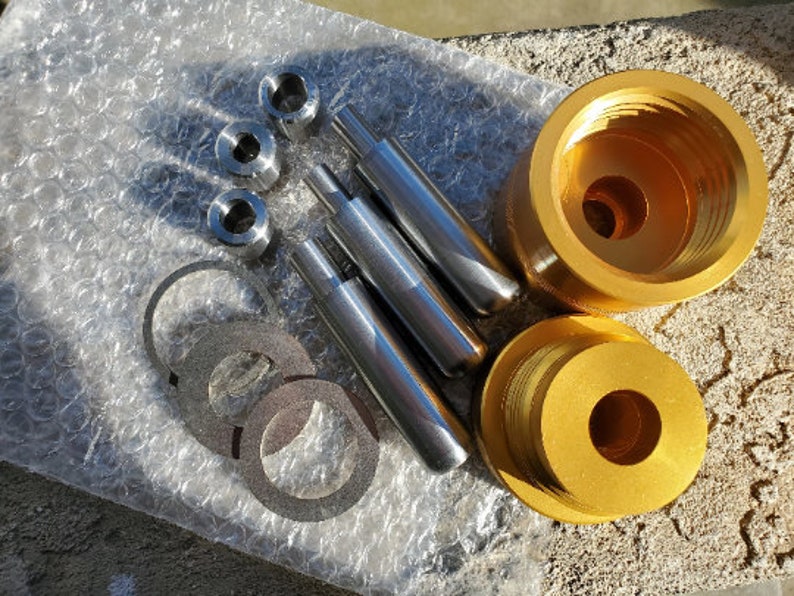May include: A set of gold metal tools for making leather crafts. The set includes a punch, a mallet, and a set of dies. The tools are laid out on a silver bubble wrap surface.