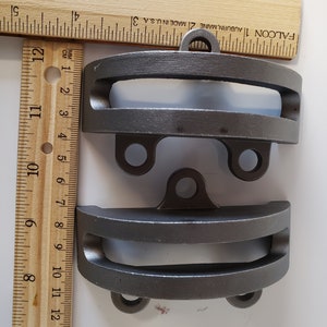 May include: Two gray metal hooks with a rounded top and a rectangular opening in the center. The hooks are about 3 inches long and have a hole at the top for hanging.