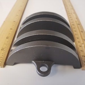 May include: Four stacked metal rings with a rounded edge and a small loop on the bottom. The rings are a dark gray color.