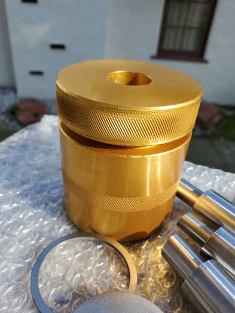 May include: Gold-colored metal tool with a threaded top and a smooth, cylindrical body. The tool is sitting on a bubble wrap surface.