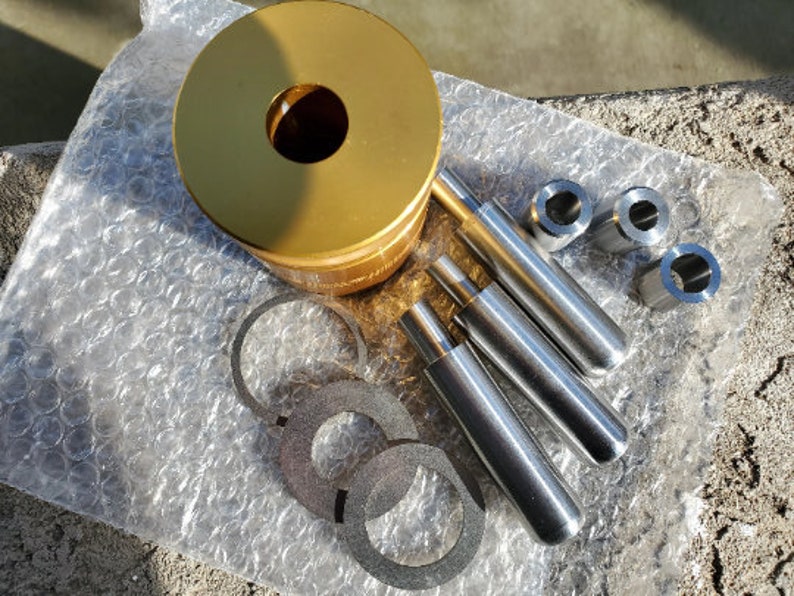 May include: A gold metal punch set with four different sized punches and a base. The punches are made of metal and have a silver finish. The base is made of gold metal and has a round shape.