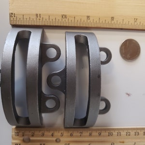 May include: Two silver metal rings with a rounded rectangular shape and two small loops on each side. The rings are about 2 inches in diameter and are measured against a ruler.