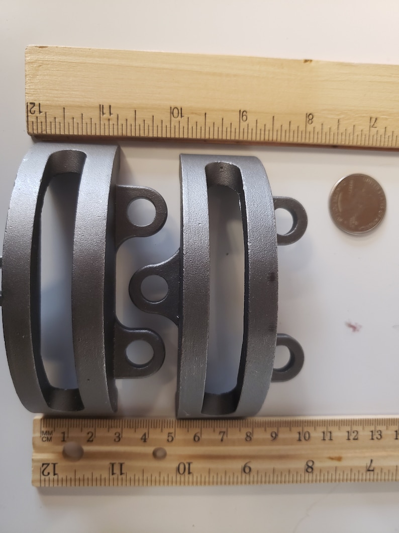 May include: Two silver metal rings with a rounded rectangular shape and two small loops on each side. The rings are about 2 inches in diameter and are measured against a ruler.