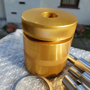 May include: Gold-colored metal tool with a threaded top and a smooth, cylindrical body. The tool is sitting on a bubble wrap surface.