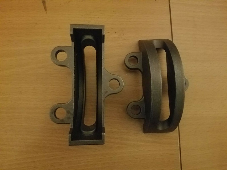 May include: Two black metal brackets with rounded edges and holes. The brackets have a slot cut out of the center.