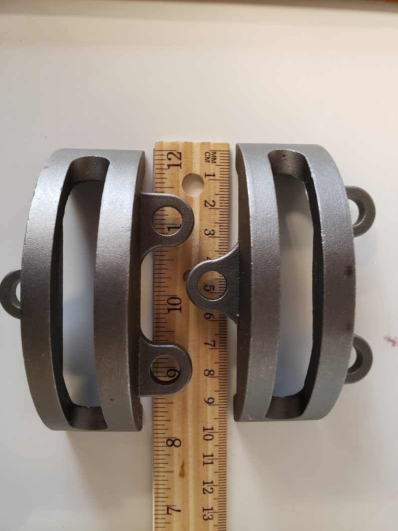 May include: Two silver metal rings with a rounded shape and a small hole at the top. The rings are about 6 inches in diameter and are measured against a wooden ruler.