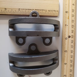 May include: Two metal gray clamps with a loop on the top and two holes on the bottom. The clamps are 1 3/4 inches long and 1/2 inch wide. The clamps are measured against a wooden ruler.