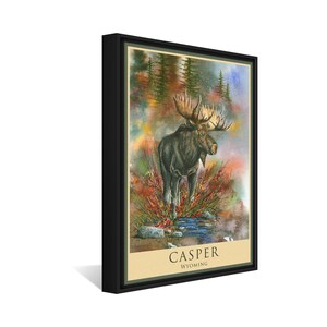 K&ouml;nnte beinhalten: Ein Aquarellbild eines Elchs, der in einem Bach steht, mit einem nebligen Wald im Hintergrund. Das Bild ist schwarz gerahmt und tr&auml;gt unten den Text "CASPER WYOMING".