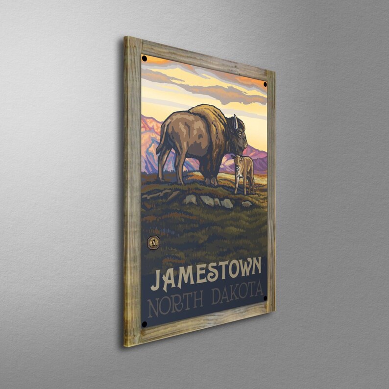 May include: A vintage-style poster with a wooden frame featuring a brown and white bison and a calf standing in a grassy field. The poster has the text "JAMESTOWN NORTH DAKOTA" at the bottom.