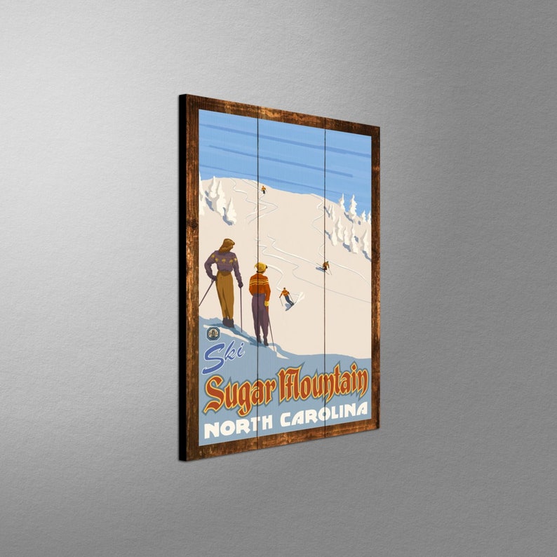 May include: Wooden framed wall art featuring a vintage ski poster for Sugar Mountain, North Carolina. The artwork depicts skiers on a snowy mountain slope with a blue sky background. The poster has a retro design with the words "Ski Sugar Mountain" and "North Carolina".