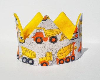 May include: A yellow and orange construction vehicle crown with a white background. The crown features a variety of construction vehicles, including dump trucks, cement mixers, and excavators.