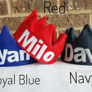 May include: Three felt crown hats in red, royal blue, and navy blue. Each hat has a white felt name embroidered on the front. The names are "Milo", "Ryan", and "David".