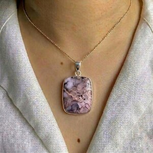 May include: A silver pendant necklace with a rectangular, pale purple stone, marbled with darker purple and white. The pendant is suspended from a fine silver chain. This necklace is a stylish piece of jewellery, suitable for everyday wear or special occasions.