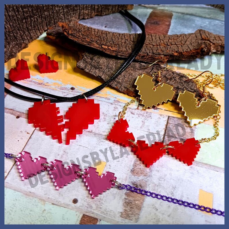 Puede incluir: Una colecci&oacute;n de joyas con forma de coraz&oacute;n, que incluye un collar con colgante de coraz&oacute;n roto, pendientes de coraz&oacute;n dorados y una pulsera de coraz&oacute;n rosa. Las joyas tienen un dise&ntilde;o pixelado. El fondo presenta madera y un borde azul.