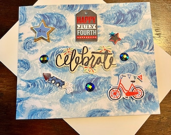 May include: A handmade greeting card with a blue and white wave pattern. Embellishments include a star, a tag that says "Happy July Fourth", the word "Celebrate", a firework, a bicycle, and iridescent gems. The card is inside a white envelope.
