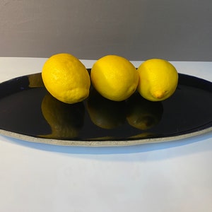 May include: Three yellow lemons on a dark blue oval ceramic serving platter with a white rim.