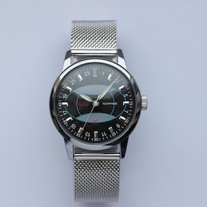 May include: A silver wristwatch with a mesh band and a black face. The watch face features a blue and red design with the word "ПОЛЯРНЫЕ" and white numerals. The watch has a silver bezel and a crown on the right side.