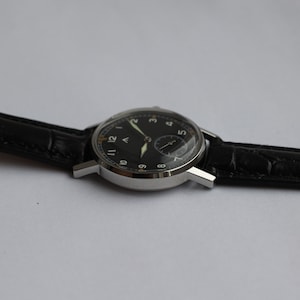 May include: A black-faced wristwatch with a silver case and black leather band. The watch face has white Arabic numerals and a small second hand.