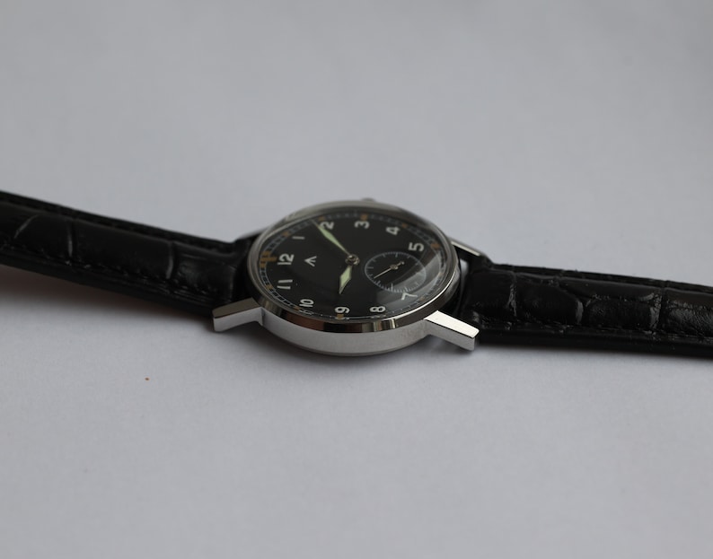 May include: A black-faced wristwatch with a silver case and black leather band. The watch face has white Arabic numerals and a small second hand.