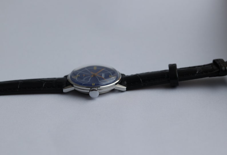 Puede incluir: Un reloj de pulsera plateado con una esfera azul y agujas doradas. El reloj tiene una correa de cuero negra.