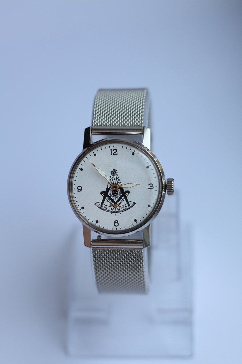 May include: A silver wristwatch with a white face and a silver mesh band. The face of the watch features a black and white compass and square design.