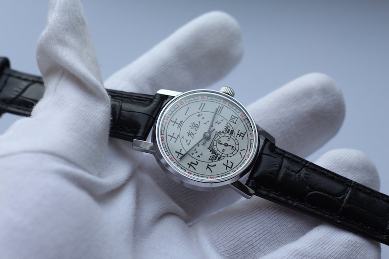 May include: A silver wristwatch with a white face and black leather band. The face features a unique design with Chinese characters and a depiction of a cityscape.