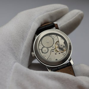 May include: A silver wristwatch with a clear case back revealing the intricate mechanical movement. The watch is on a black leather strap.