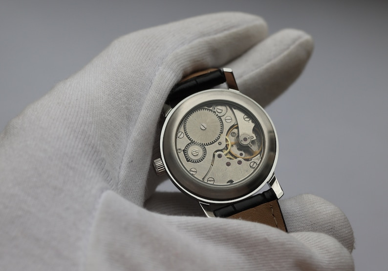 May include: A silver wristwatch with a clear case back revealing the intricate mechanical movement. The watch is on a black leather strap.