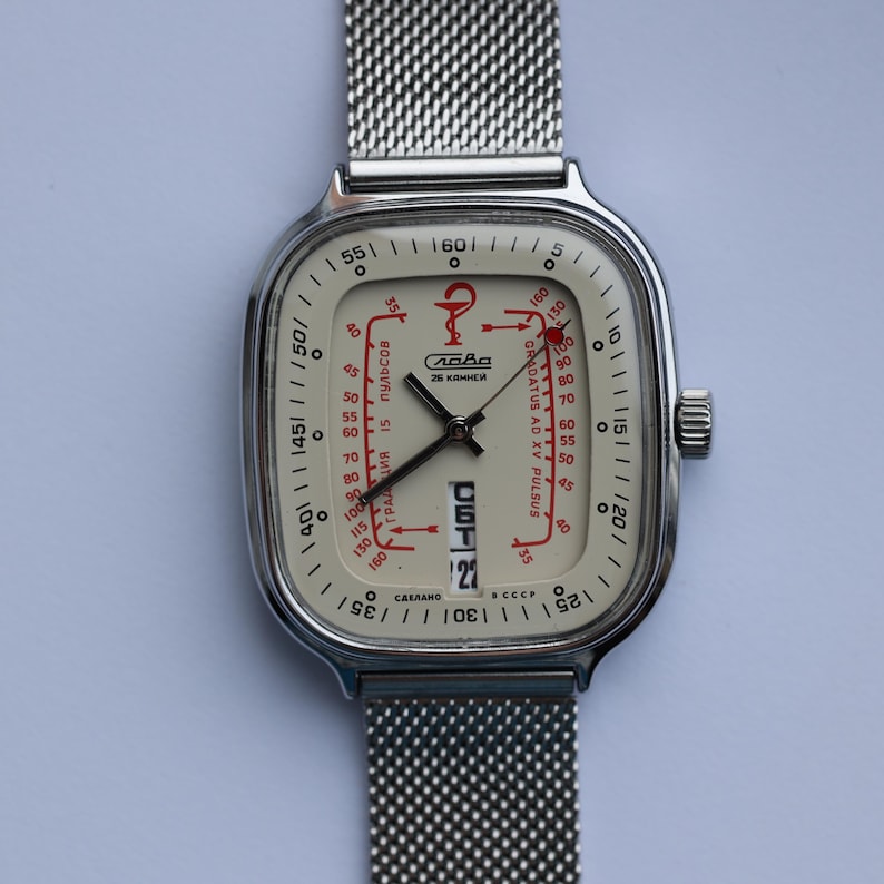 May include: A vintage wristwatch with a square, cream-colored face and a silver mesh band. The watch face features red accents, including text and a medical symbol. The date is displayed at the bottom. The watch is a unique accessory.