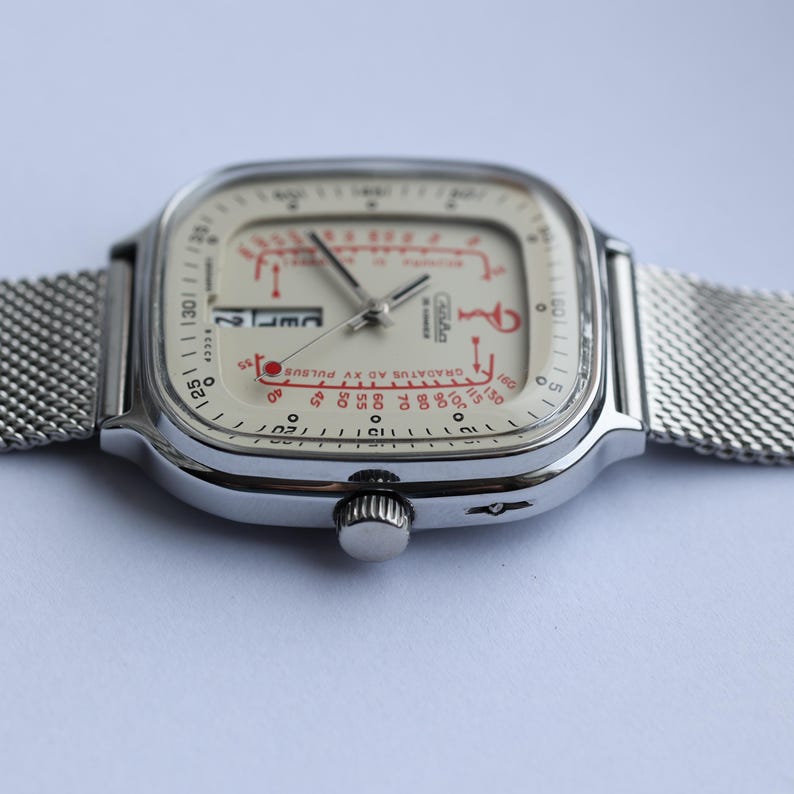 May include: A vintage silver wristwatch with a mesh band. The watch face is off-white with red and black markings, including the text "GRADATUS AD XV PULSUS". The watch has a square face with rounded corners and a small date window.
