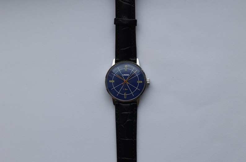 Puede incluir: Un reloj de pulsera plateado con una esfera azul y detalles dorados. El reloj tiene una correa de cuero negra.